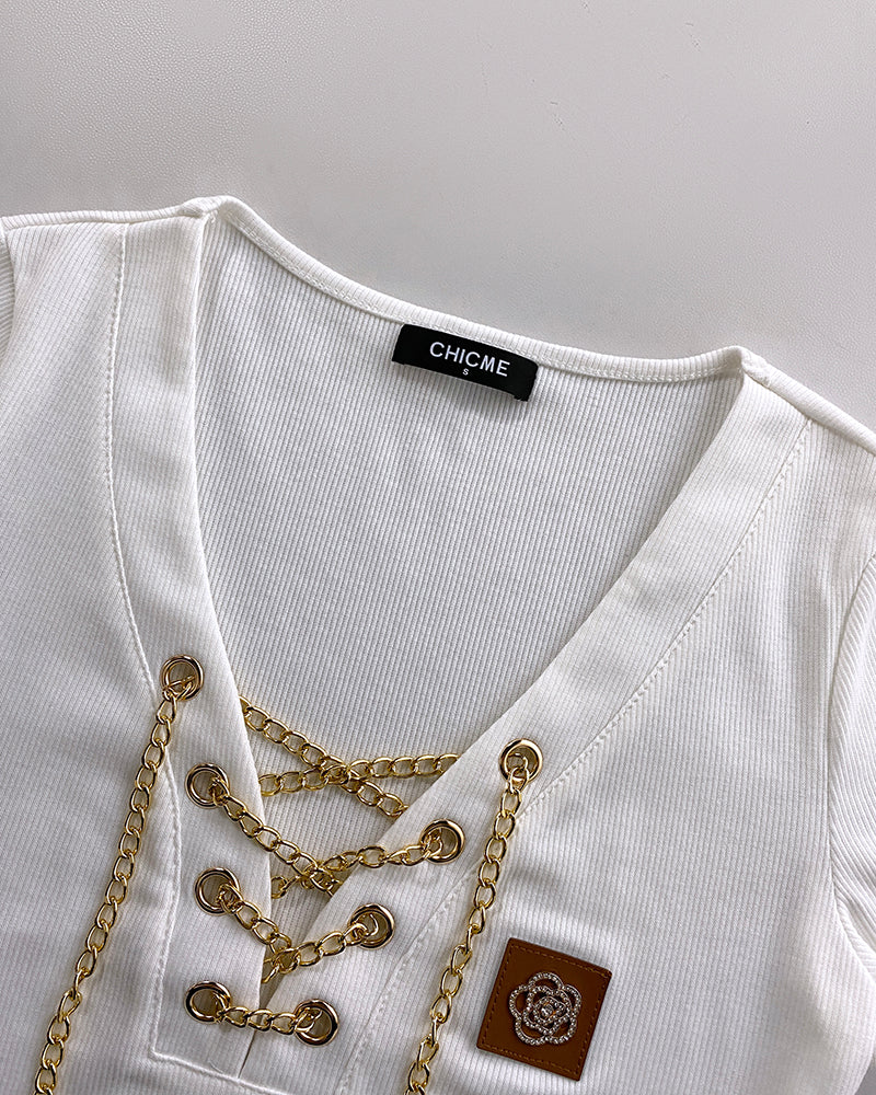 White ribbed V-neck T-shirt with lace-up detail, rhinestones, and chest emblem patch.