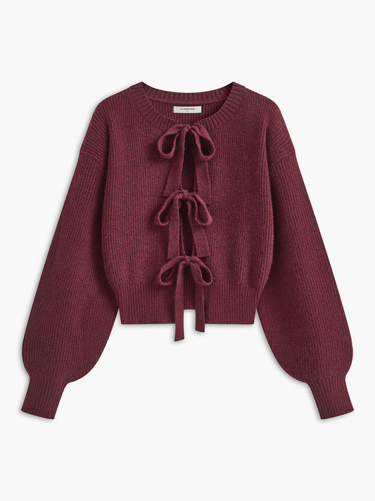 A maroon cropped knit cardigan with lace trim, ribbed texture, three bows, and balloon sleeves.